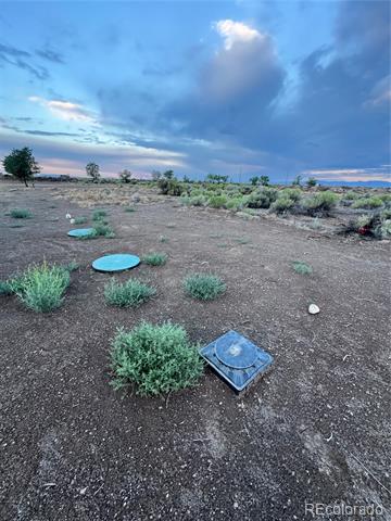 Open rural parcel with scattered shrubs and utility covers beneath a cloudy sky.