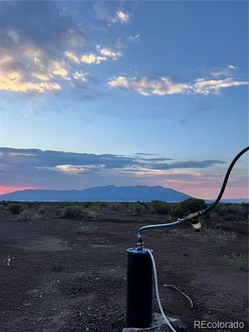 Rural property with a water well pump in the foreground and mountains at dusk.