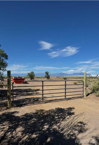 Metal gate across a dirt road leading into open rural acreage, with distant mountains.