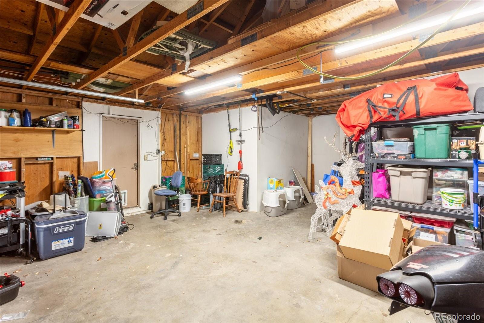 Garage with exposed wooden ceiling framing, storage shelves, and a concrete floor.