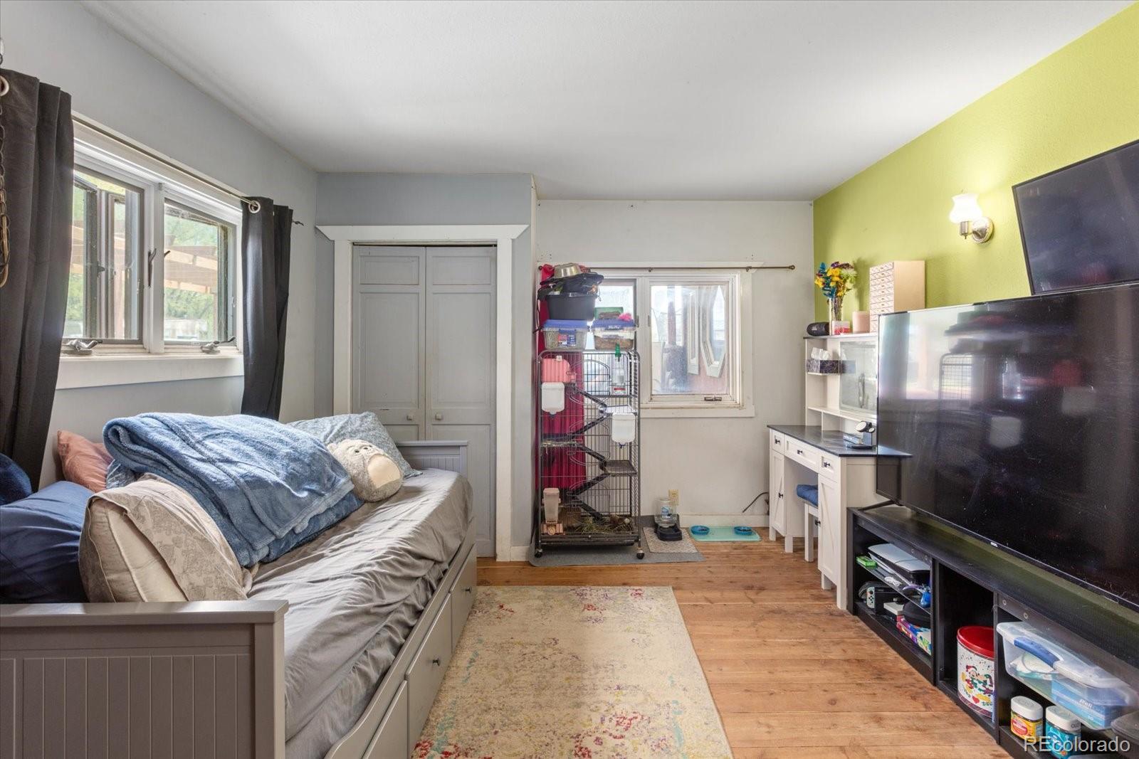 Bedroom with a gray bed, wood flooring, lime-green accent wall, and large televisions.