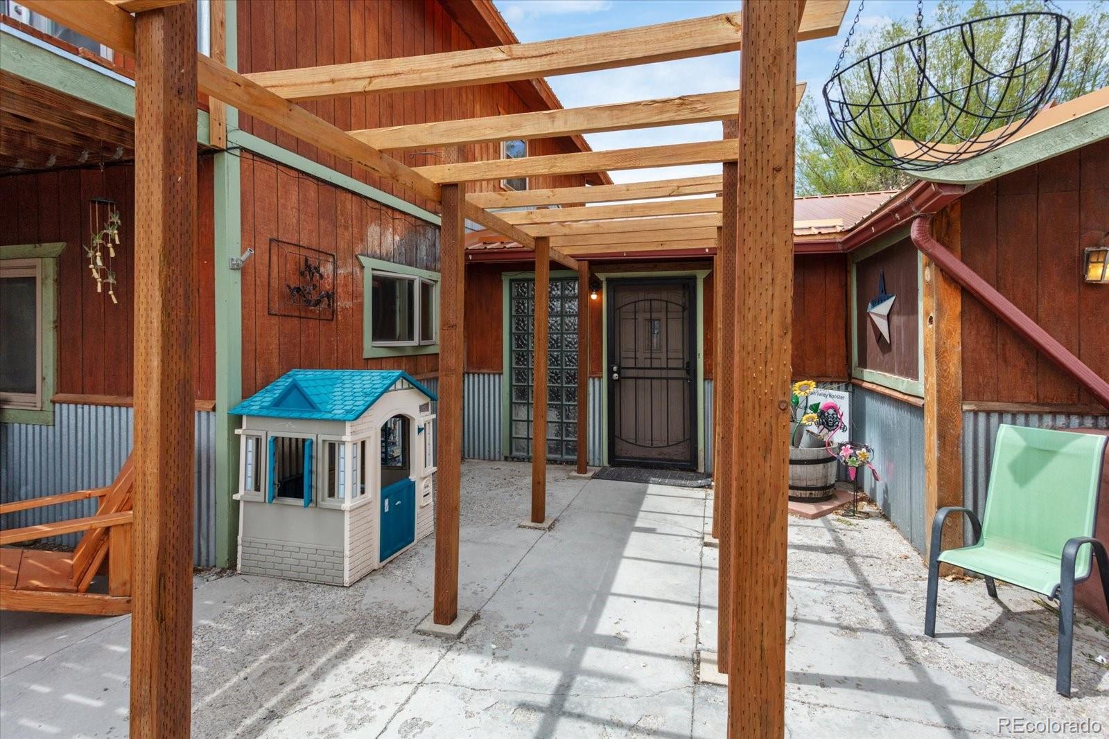 Covered courtyard entry with a timber pergola, dark front door, and colorful playhouse.