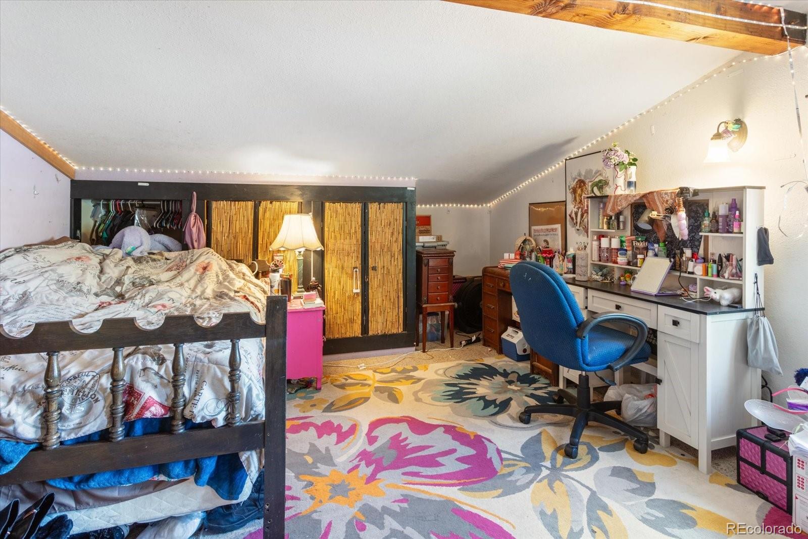 Bedroom with a large bed, bamboo closet doors, and a desk beneath a sloped ceiling.