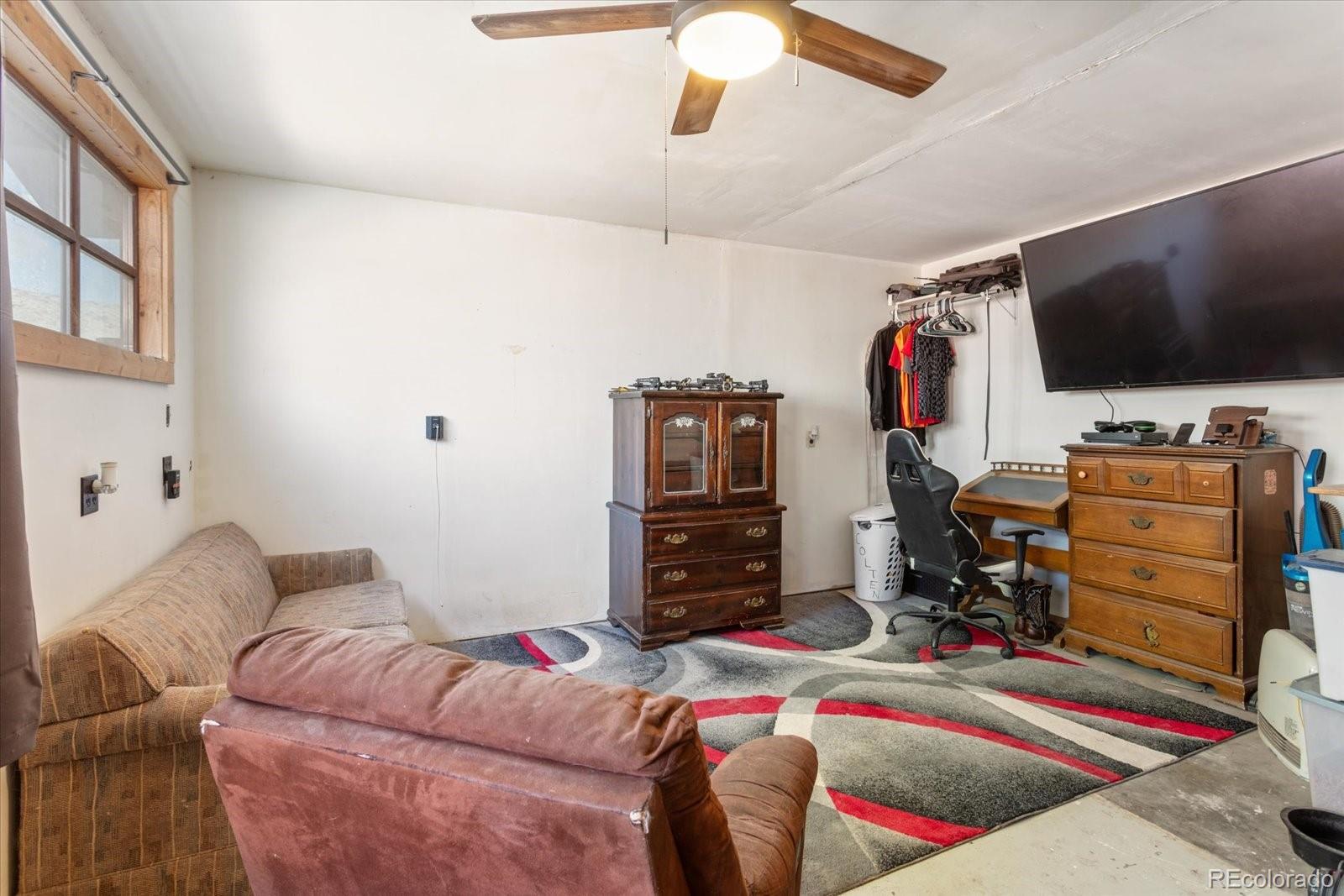 Furnished living room with a ceiling fan, patterned rug, and wall-mounted television.