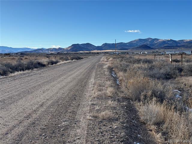 Dirt access road crossing dry scrubland toward distant mountains.