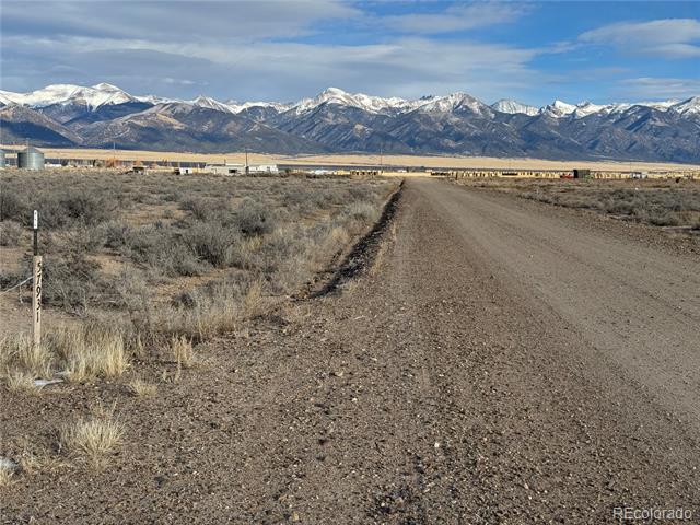 Open scrubland and a gravel road lead toward snow-dusted mountains.