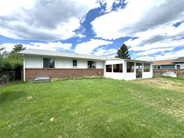 Rear of a single-story ranch house with brick siding, enclosed patio, and broad lawn.