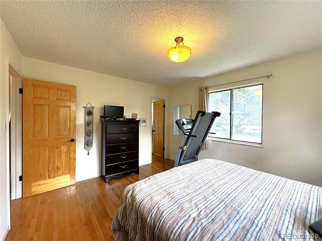 Bedroom with hardwood floors, a dark dresser, and a treadmill beside the window.