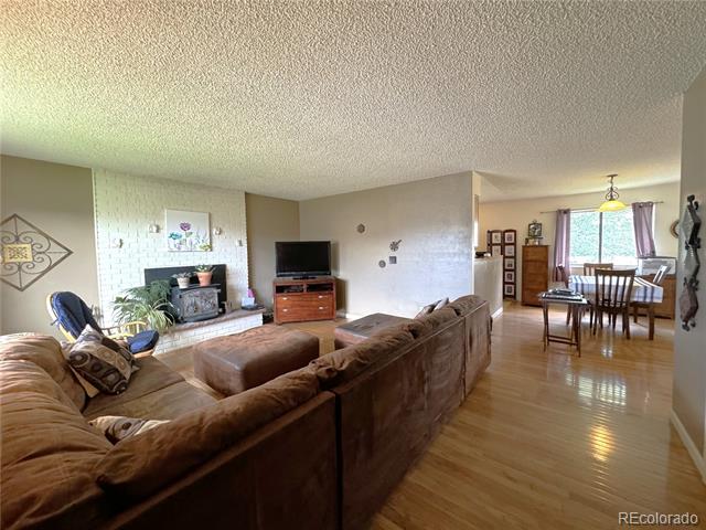Living room with a brown sectional, brick fireplace, wood flooring, and an adjoining dining area.