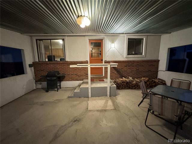 Enclosed covered patio with a corrugated ceiling, brick half walls, patio chairs, and stacked firewood.