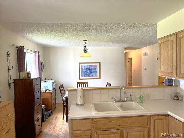 Kitchen with a double-basin sink and light wood cabinets overlooking a dining area.