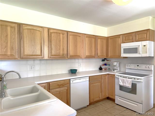Kitchen with honey-colored wood cabinets, white counters, and a double-basin sink.