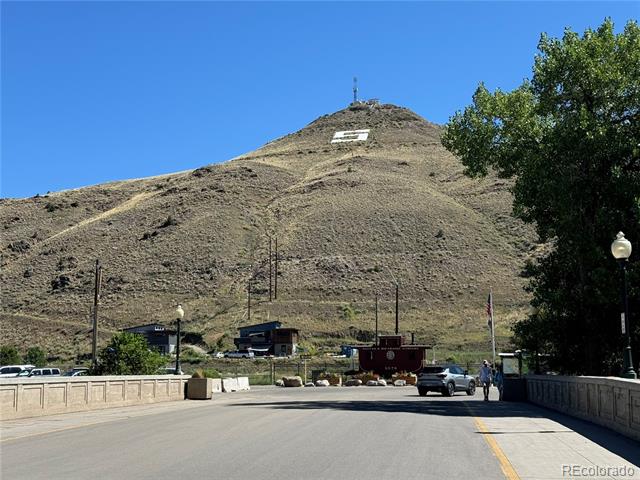 Road and bridge leading toward a dry hillside with a white marking near the summit.