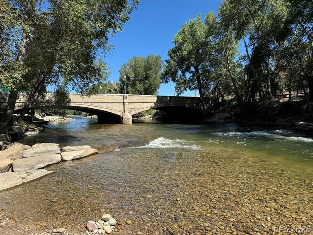Stone bridge over a shallow, rocky river beneath leafy trees.
