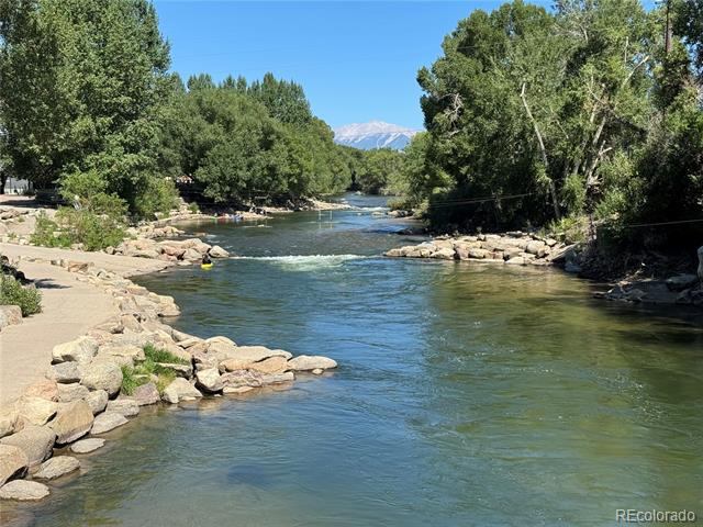 River bordered by rocky banks and green trees, with a snow-capped mountain in the distance.