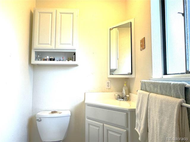 Bathroom with a mirrored vanity, white toilet, wall cabinet, and towels beside a large window.