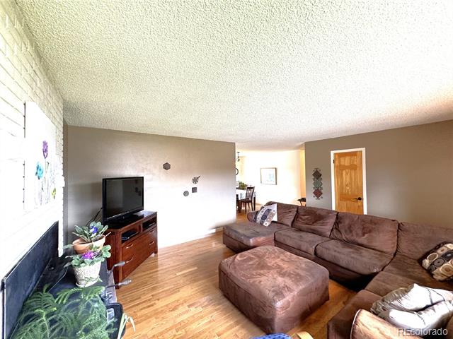 Living room with a brown sectional, wood flooring, television, and white brick fireplace.