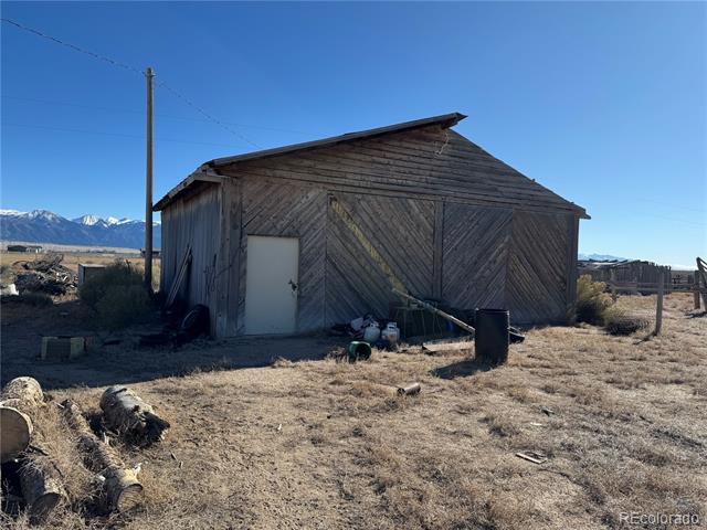 Weathered wooden outbuilding with a white door and snow-capped mountains in the distance.
