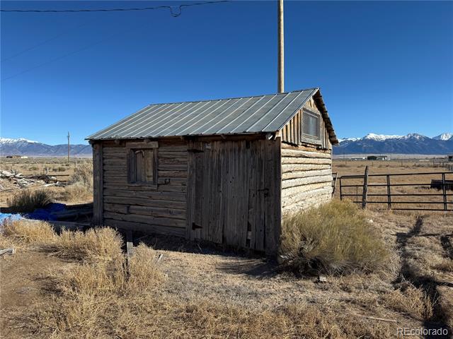 Weathered log outbuilding with a metal roof and snow-capped mountains behind it.