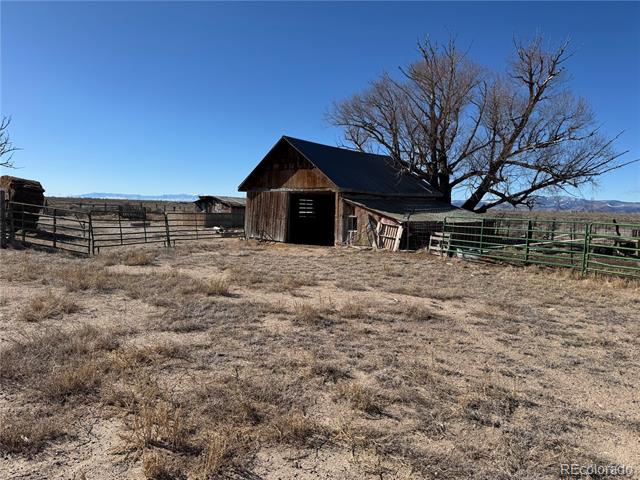 Weathered wooden barn and fenced dry pasture beside a leafless tree, with mountains in the distance.