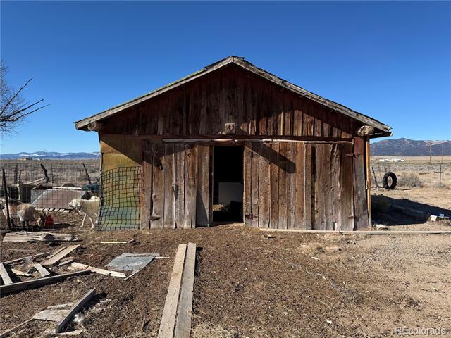 Weathered wooden outbuilding with an open doorway, scattered boards, and distant mountains.