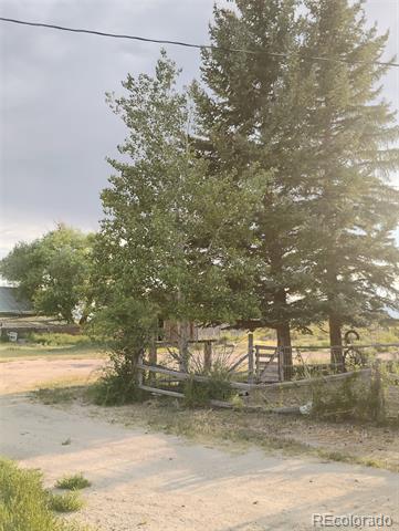 Rural property entrance with a gravel driveway, wooden fence, and mature trees.