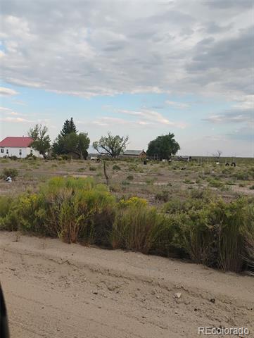 Rural scrubland beside a dirt road, with distant buildings and trees.