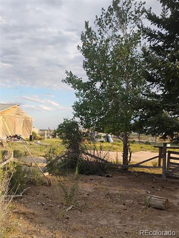 Rural property with a fenced yard, mature trees, and a partially framed wooden structure.