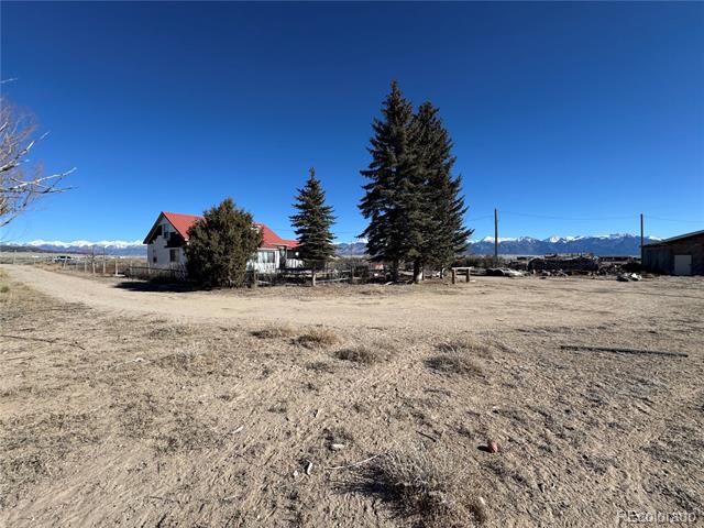 Rural house with a red roof and tall evergreens, set before distant snow-capped mountains.