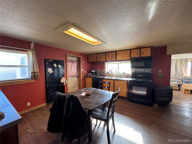 Kitchen and dining area with burgundy walls, wood cabinets, and a black refrigerator and range.