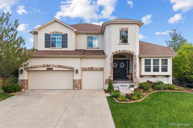Two-story cream home with brick accents, two garages, and a landscaped front lawn.