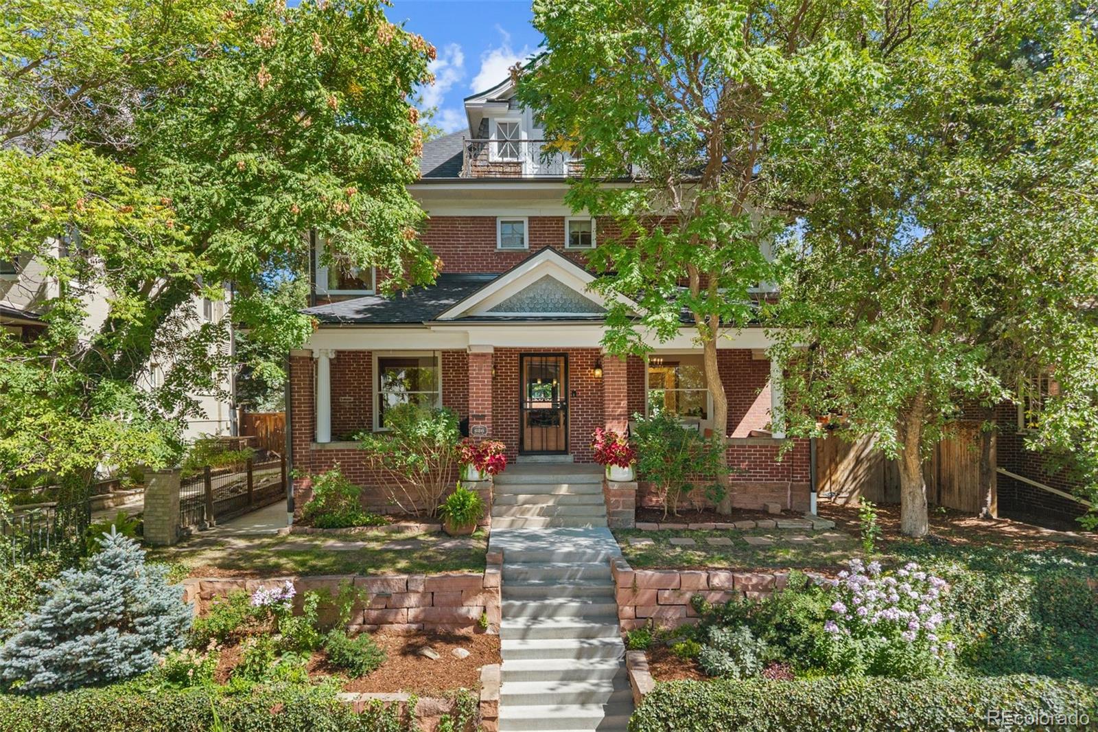 Red brick house with a covered porch, front staircase, and leafy garden.