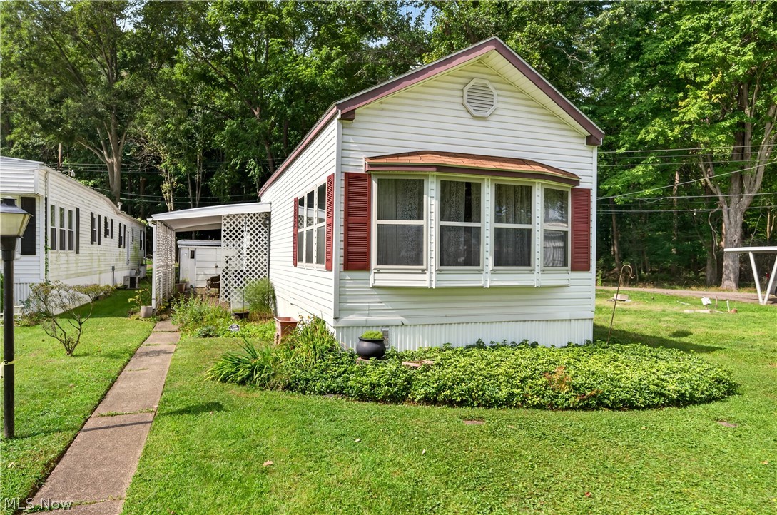 White manufactured home with red shutters, a broad front window, and a walkway through a grassy yard.