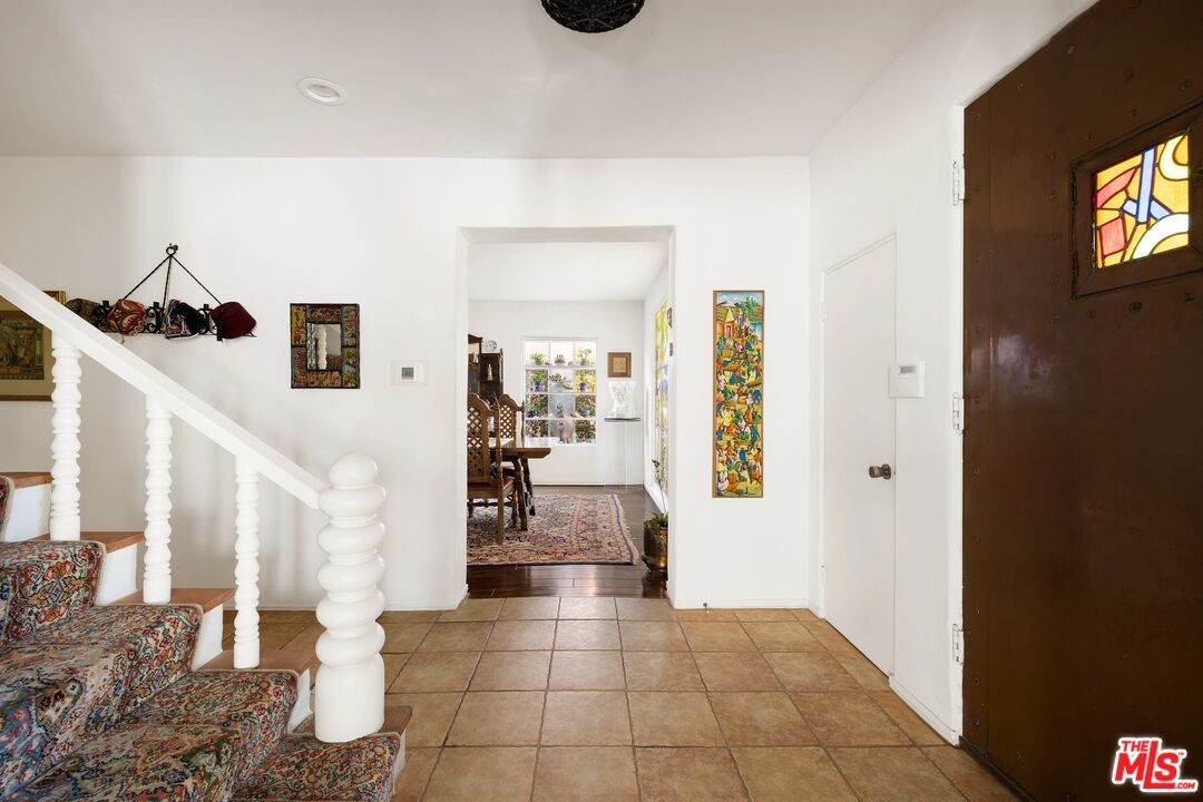 Entry foyer with a tiled floor, carpeted staircase, and dark wood door with stained glass.