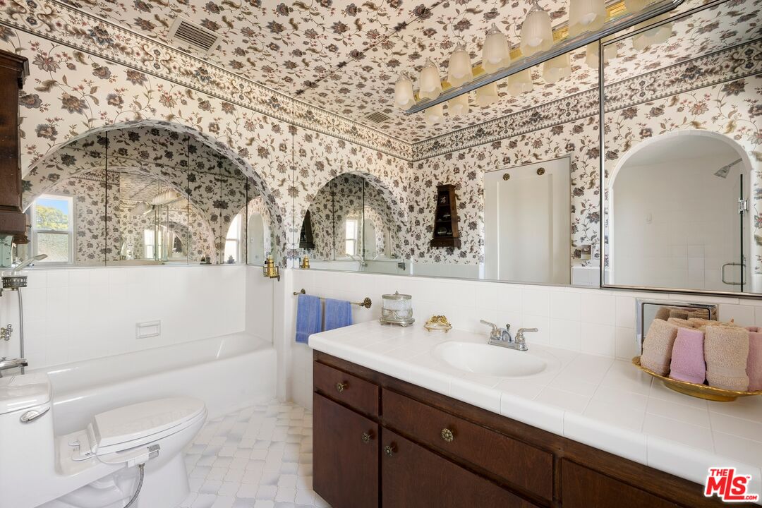 Bathroom with floral wallpaper, mirrored walls, a white tub, and a dark wood vanity.