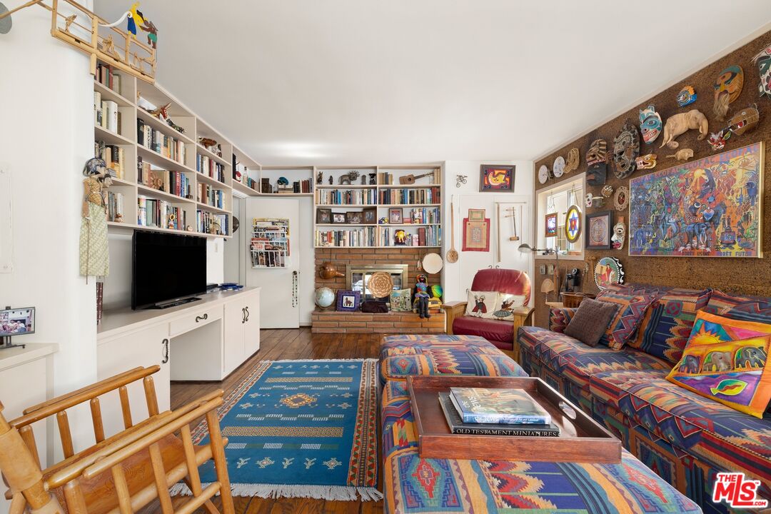 Living room with extensive bookshelves, a brick fireplace, and colorful patterned seating.