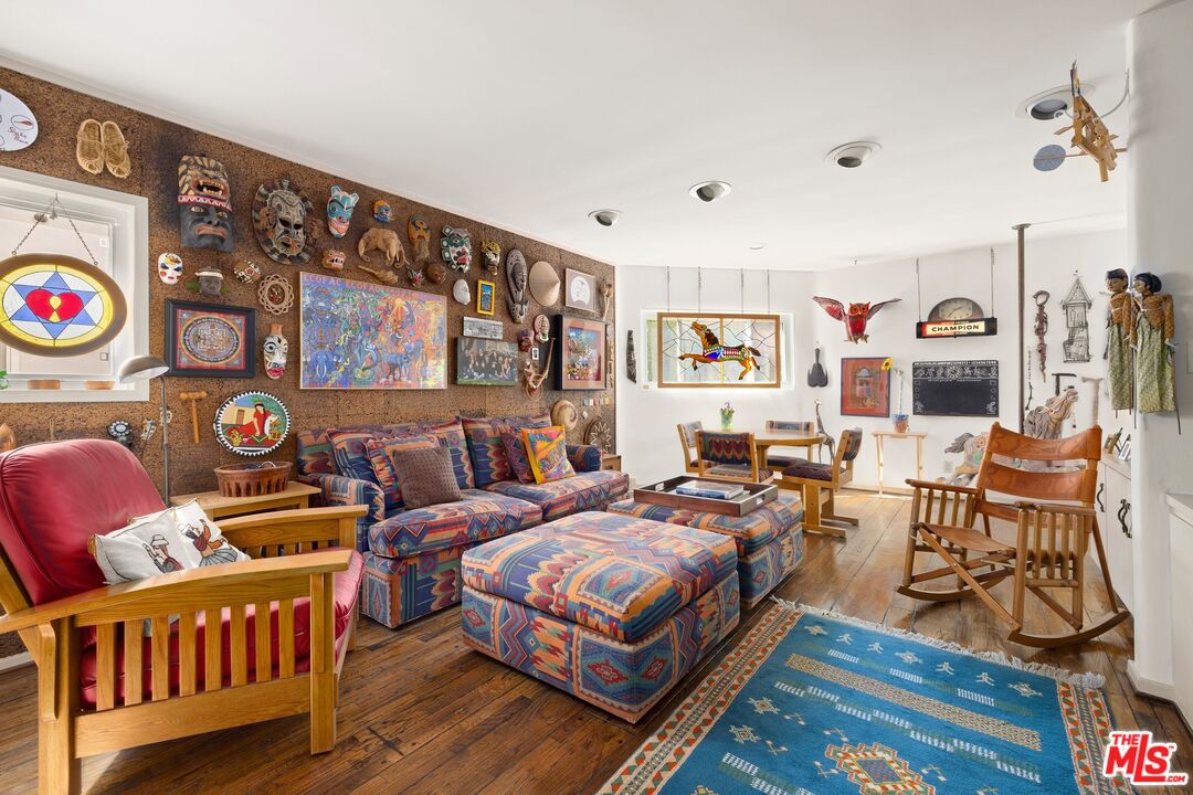 Eclectic living room with patterned seating, wood floors, a blue rug, and walls covered in masks and artwork.