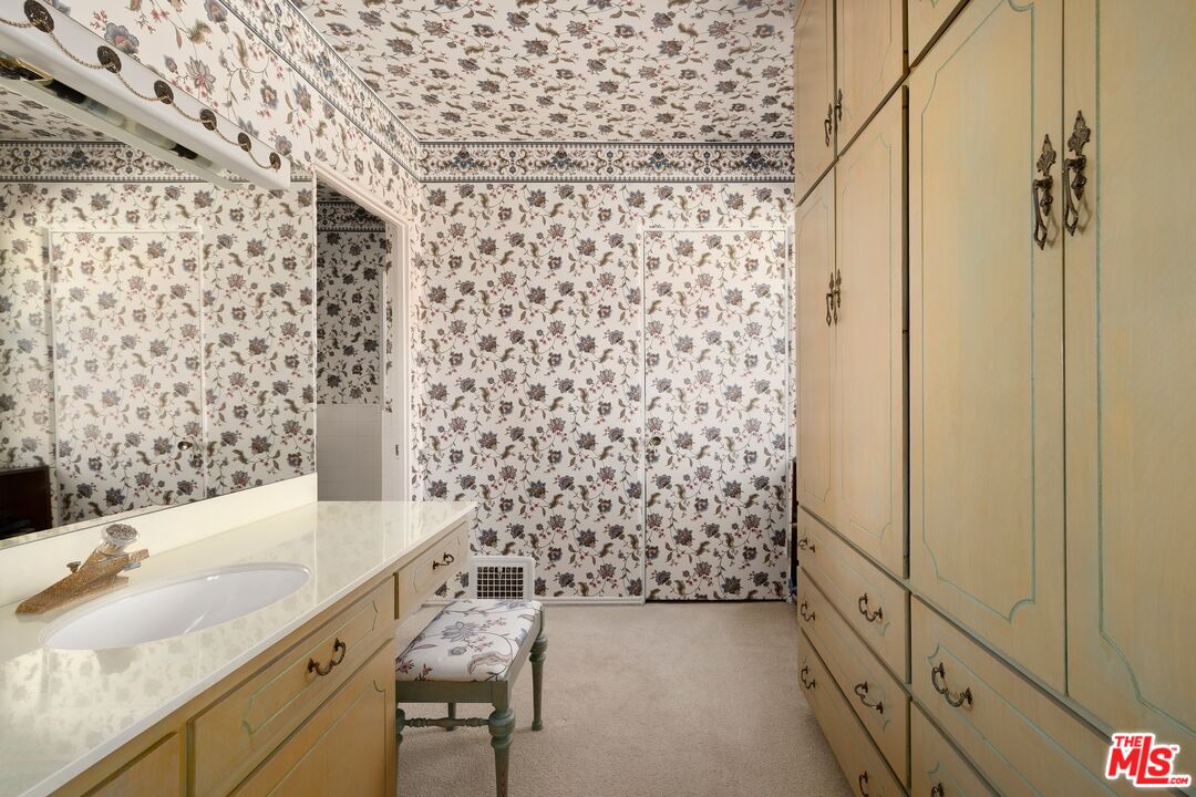 Bathroom with floral wallpaper, a long vanity, and built-in cream cabinetry.