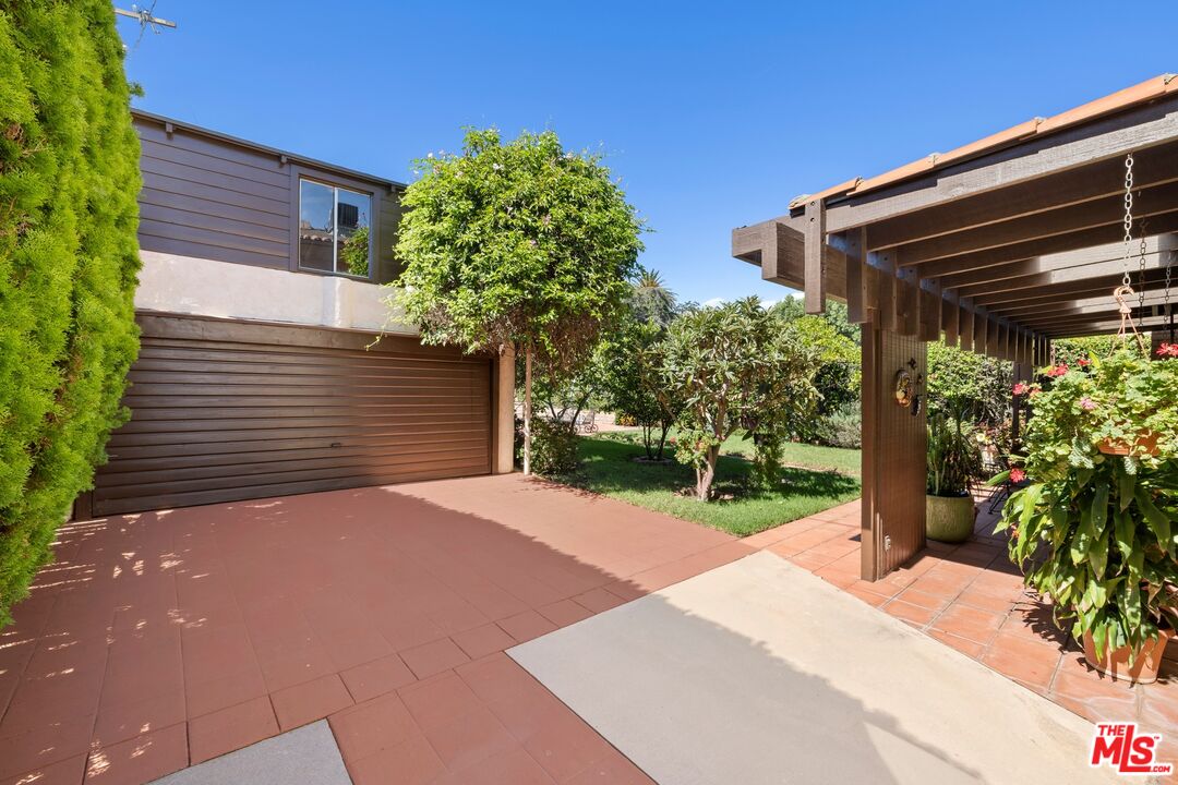 Home exterior with a wide garage, landscaped garden, and wooden pergola patio.