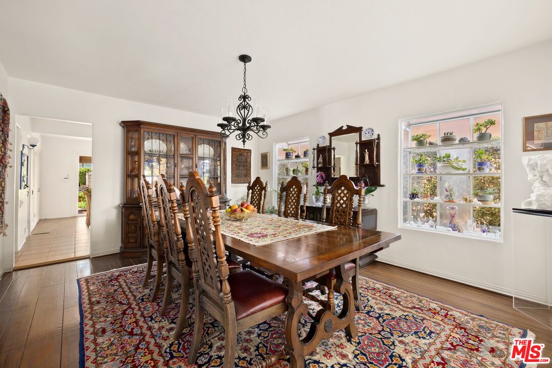 Dining room with carved wooden table and chairs, patterned rug, china cabinet, and bright windows.