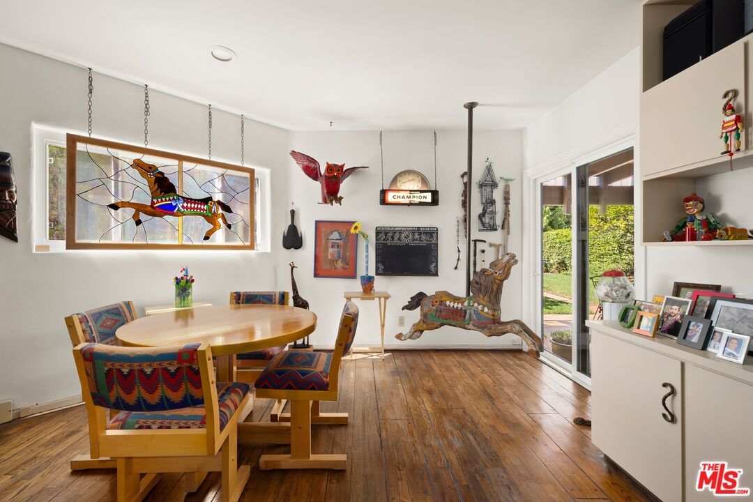 Dining room with a round wooden table, colorful chairs, stained-glass art, and sliding doors to the garden.