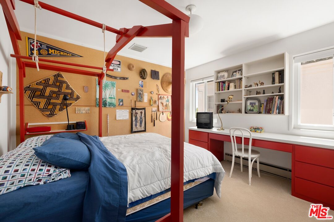 Bedroom with a red four-poster bed, blue bedding, and built-in bookshelves above a red desk.
