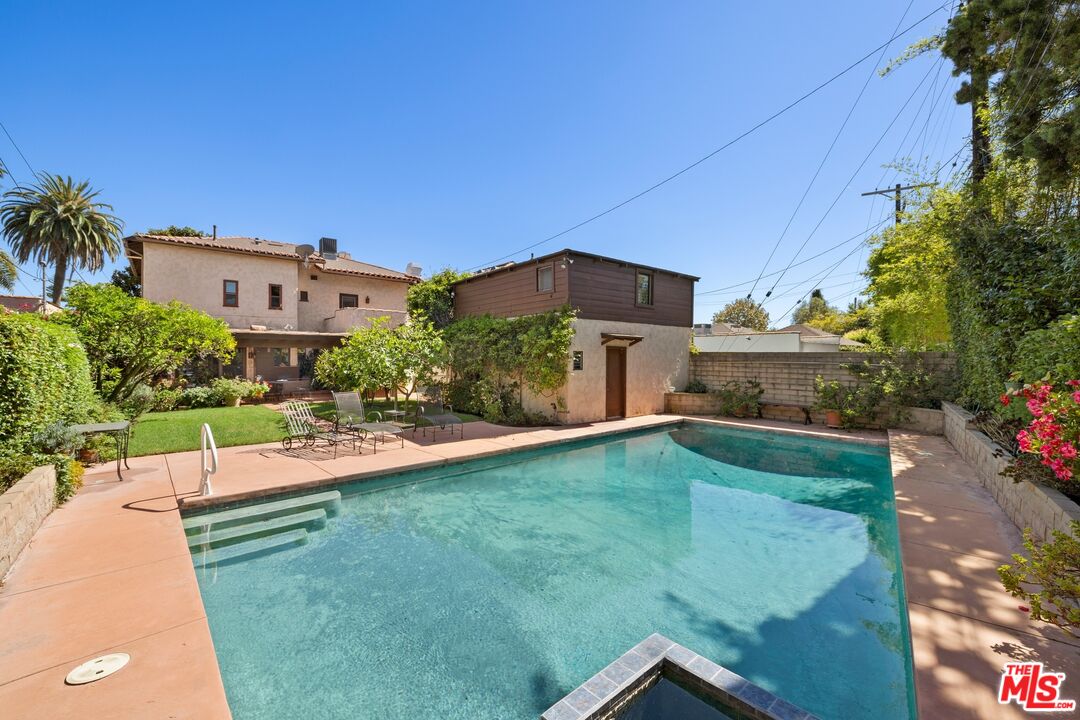 Backyard swimming pool with a paved deck, garden seating, and the house in the background.