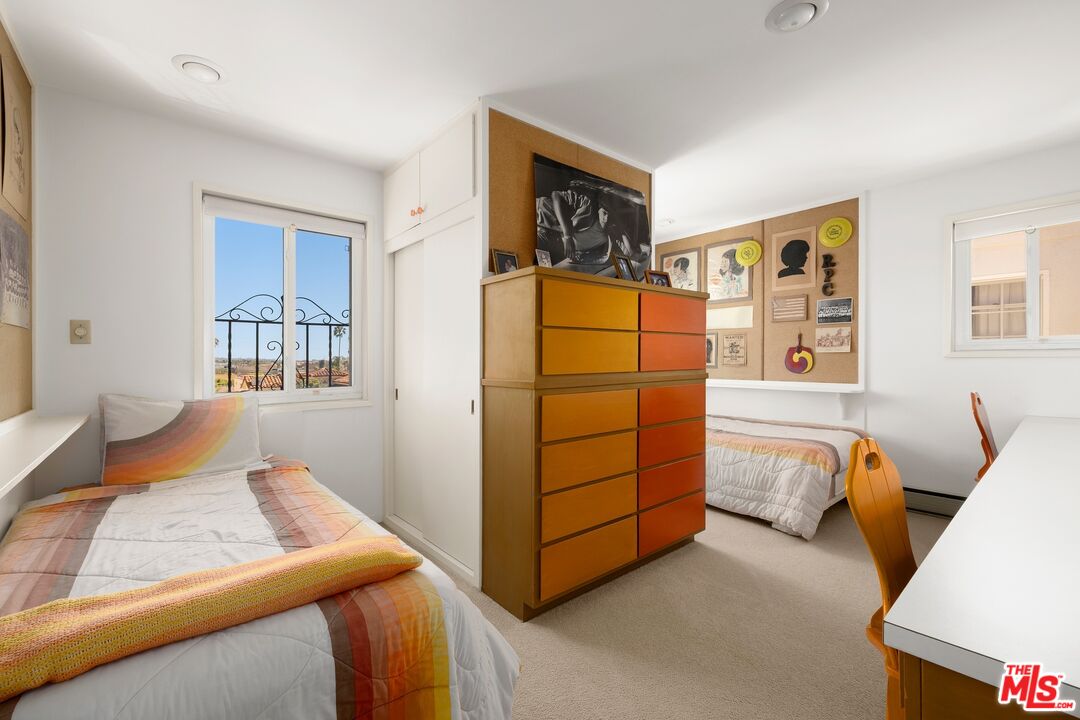 Bedroom with two single beds, colorful striped bedding, and a large orange-and-wood dresser.