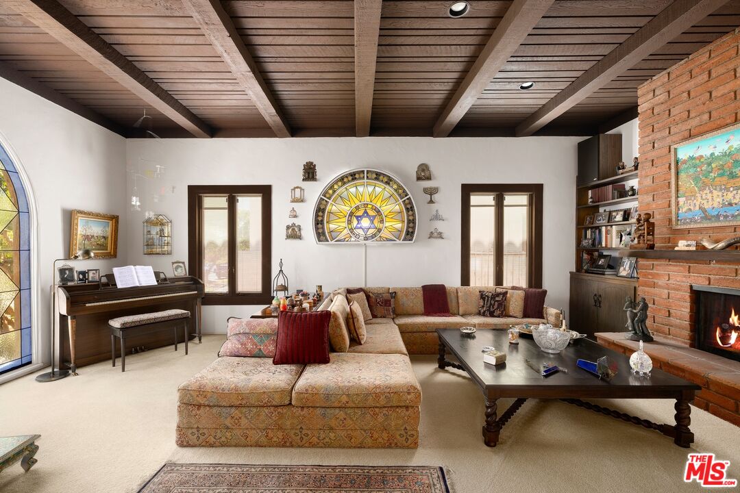 Living room with a wood-beam ceiling, brick fireplace, stained glass, and piano.