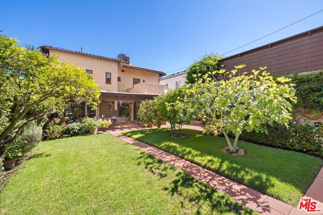 Landscaped backyard with a broad lawn, brick walkway, mature trees, and covered patio seating.