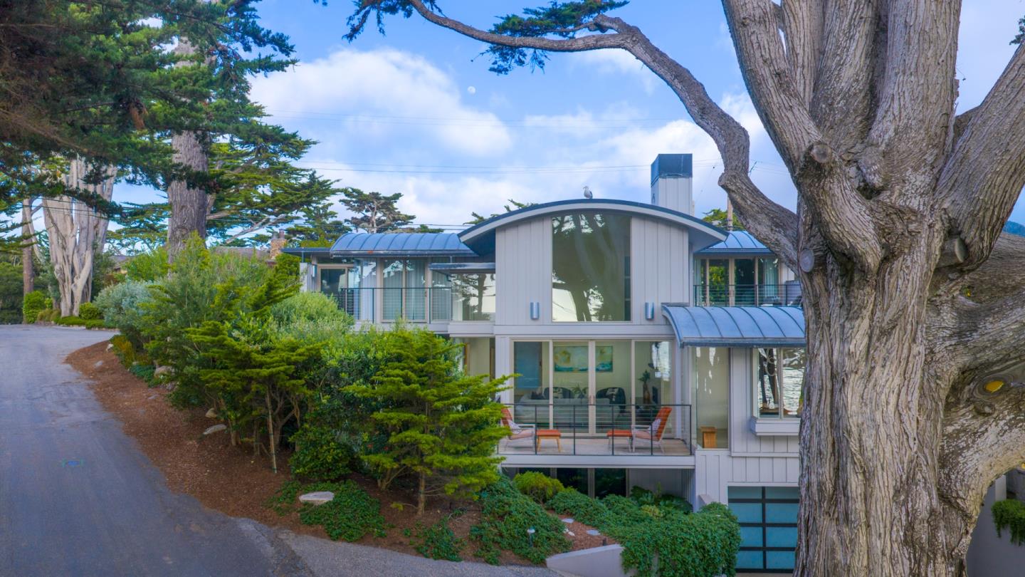 Modern two-story home with a curved roof and balconies, framed by mature trees.