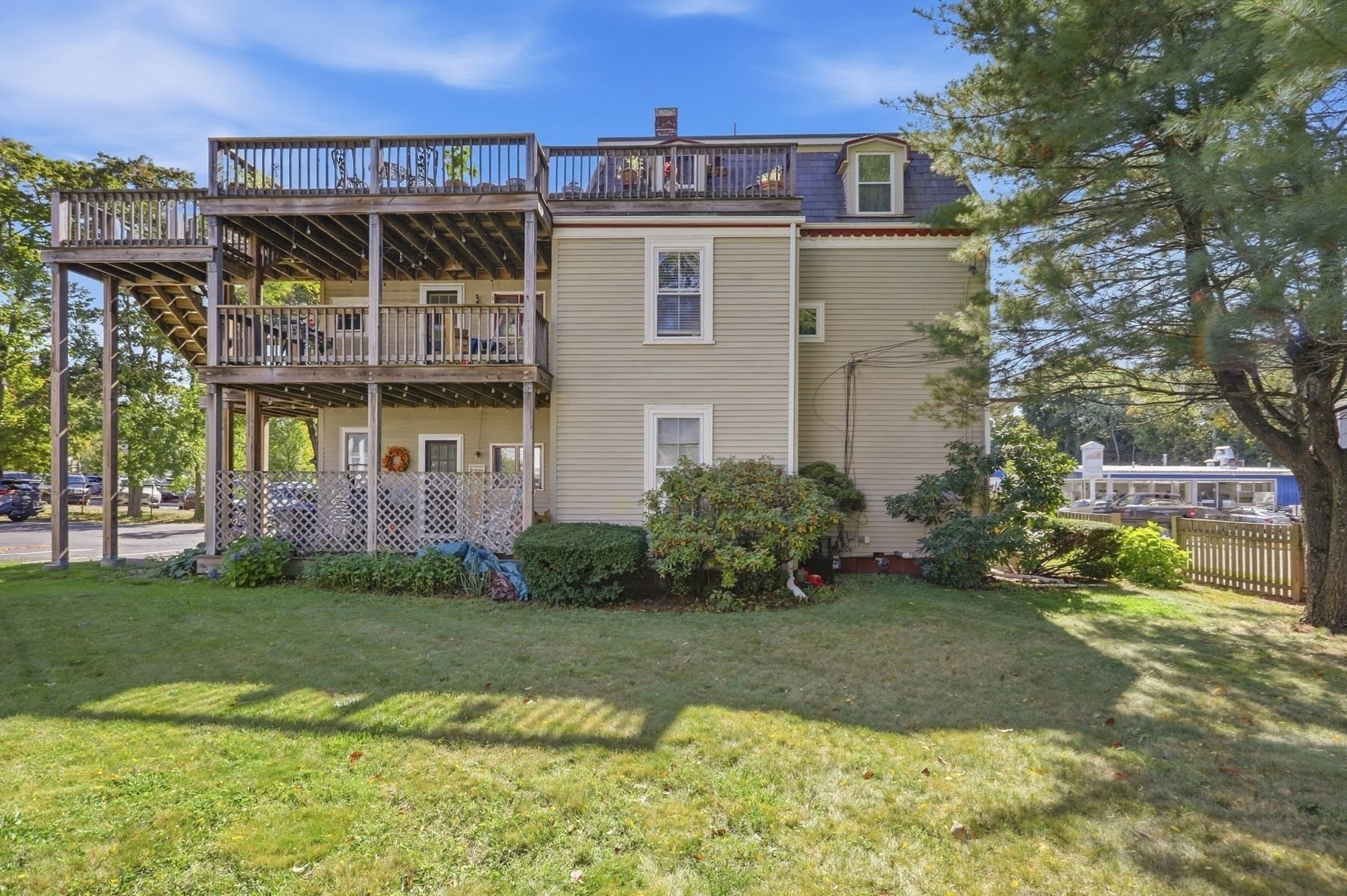 Multi-story beige home with expansive wooden decks overlooking a sunny lawn.