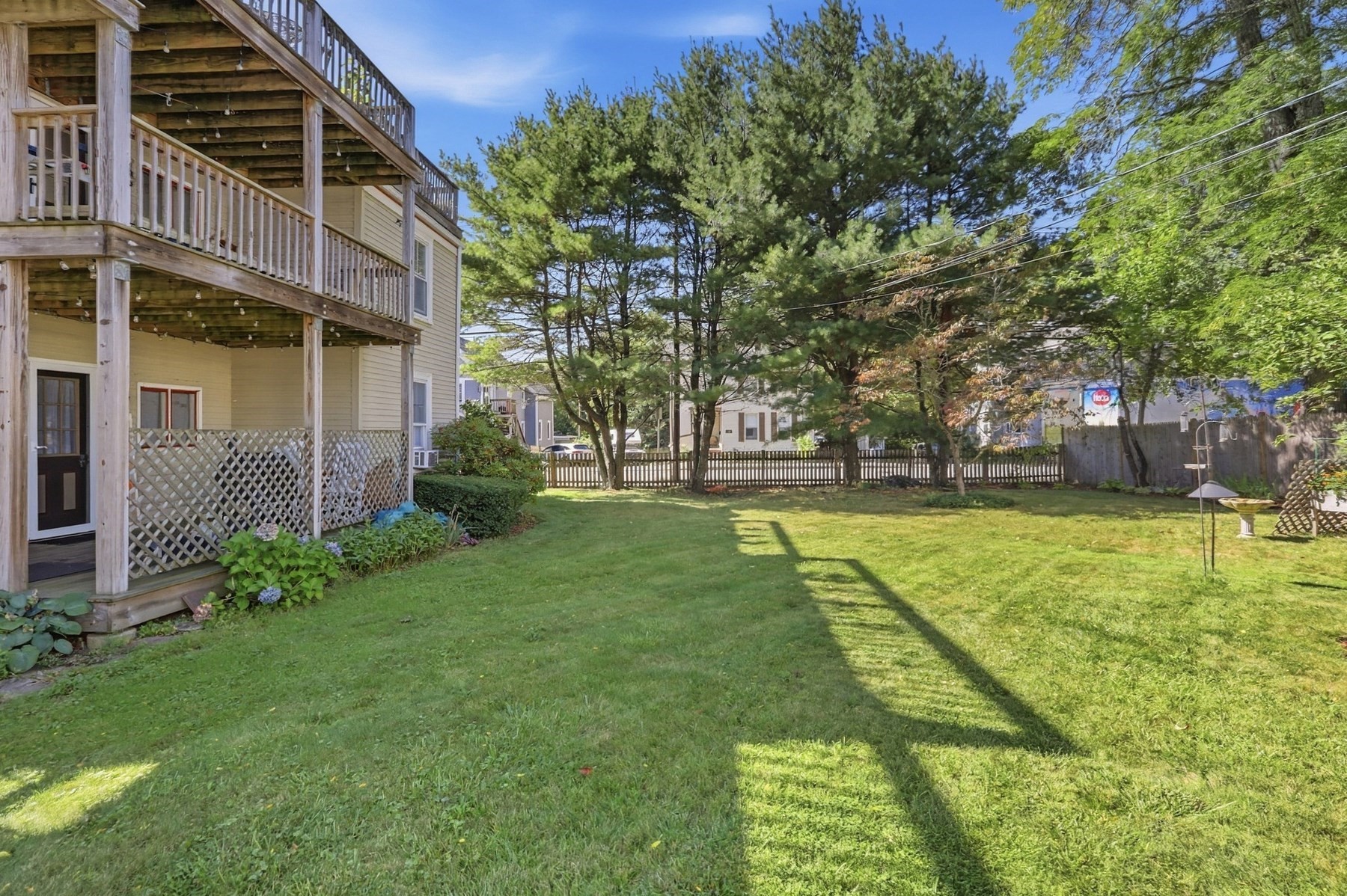 Backyard lawn beside a home with two elevated wooden decks and mature shade trees.