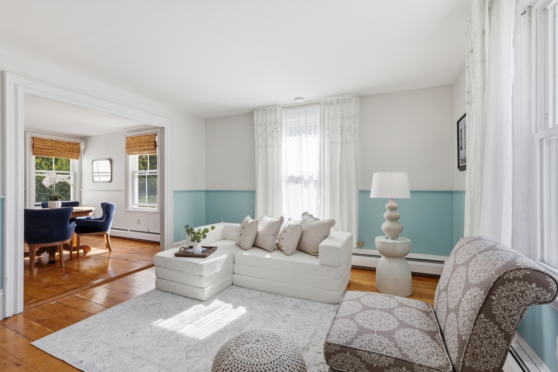 Living room with turquoise wainscoting, white sectional sofa, patterned chaise, and adjoining dining area.